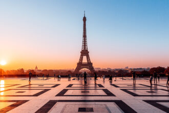 An orange sun reflects light on the smooth plaza in front of the Eiffel Tower in Paris.