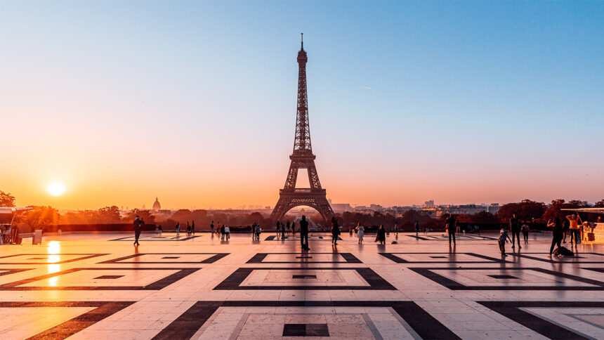 An orange sun reflects light on the smooth plaza in front of the Eiffel Tower in Paris.