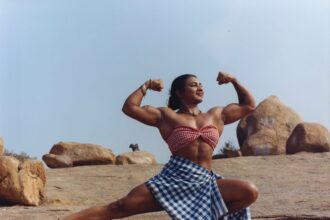 an indian woman in a a small checked bandeau top and blue and white checked skirt shows off her large muscles in a squat