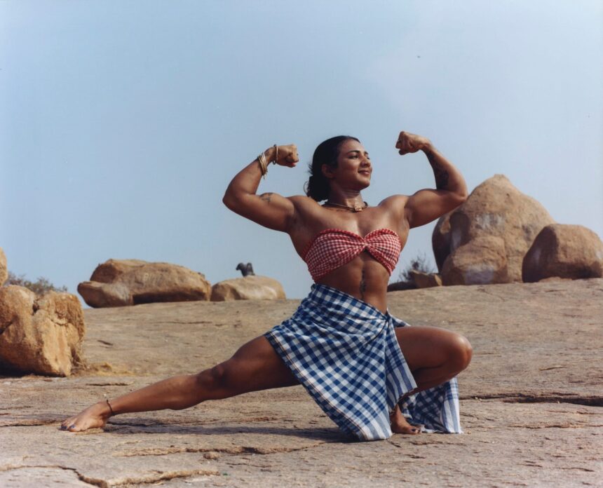 an indian woman in a a small checked bandeau top and blue and white checked skirt shows off her large muscles in a squat