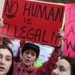 A woman holds up a sign reading "no human is illegal" at a 2017 protest in Miami.