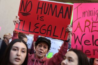 A woman holds up a sign reading "no human is illegal" at a 2017 protest in Miami.