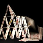 A house of cards collapsing on dark background