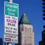 Close-up of a sign announcing congestion pricing tolls in New York City, with a blue sky and building in the background