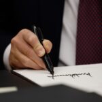 Close-up of hand holding a sharpie and signing a piece of paper