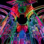 a detail of a vibrantly colored architectural pavilion made of metal poles and rope at night