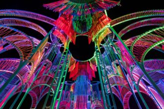 a detail of a vibrantly colored architectural pavilion made of metal poles and rope at night