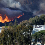 Photo of flames erupting into a dark sky behind homes on a hillside