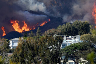 Photo of flames erupting into a dark sky behind homes on a hillside