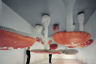 people stand in a gallery with large red-topped mushrooms sprouting from the ceilign